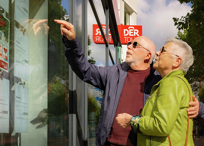 Ältere Personen zeigen auf Reisebüro Schaufenster